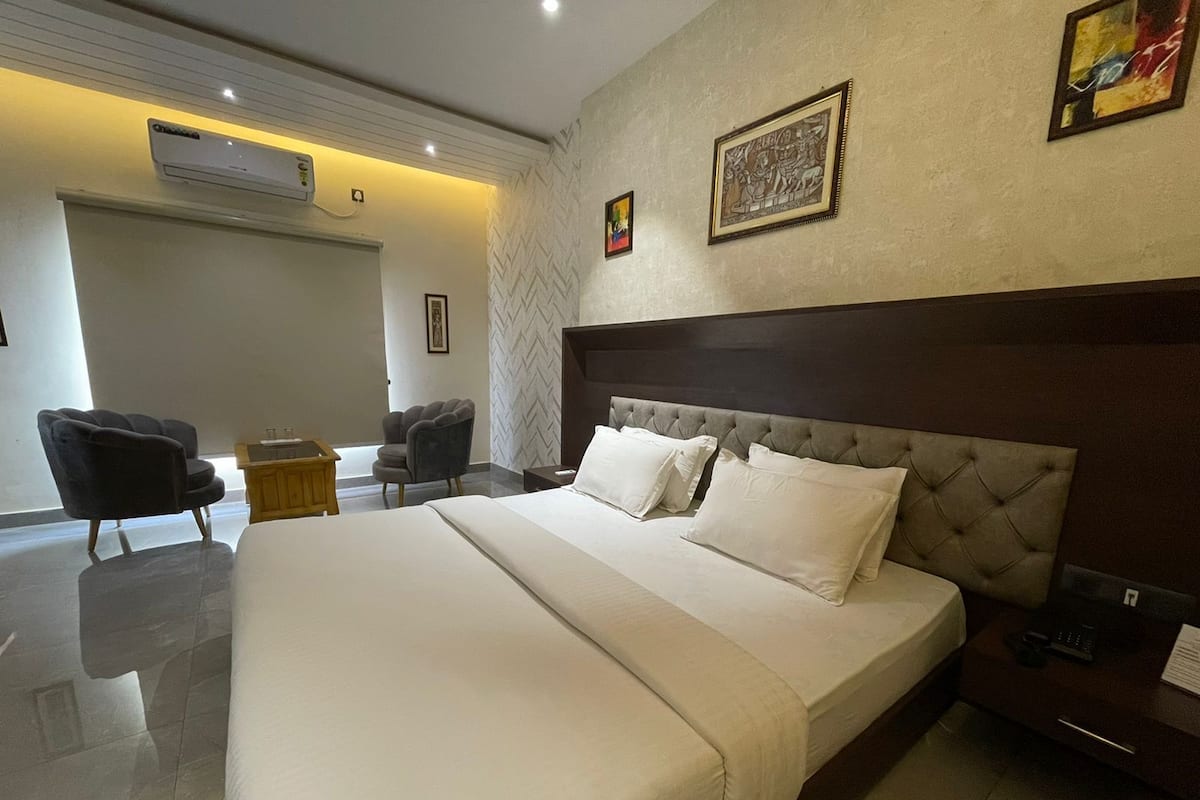 Une chambre d’hôtel avec un grand lit, deux fauteuils, une petite table et un climatiseur fixé au mur.