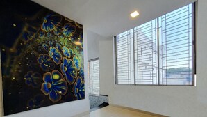 Een ruime hal met een groot bloemenmural op een muur, een raam met zonwering en een betegelde vloer.