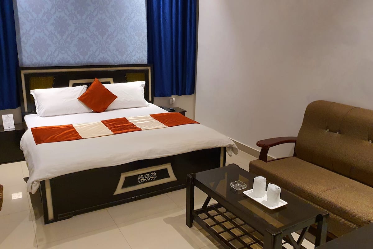 Une chambre d’hôtel avec un lit, un canapé marron, une petite table et une fenêtre avec des rideaux bleus.