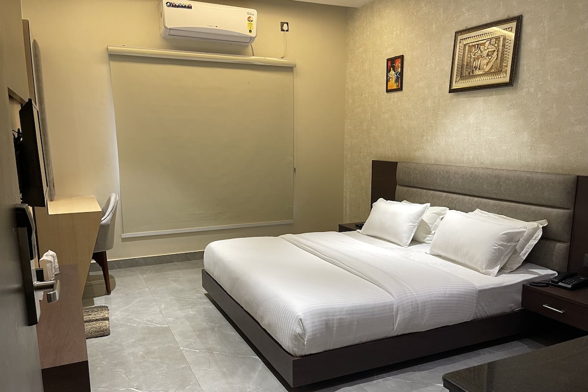 Une chambre d’hôtel comprenant un lit, une table de chevet, une commode, un climatiseur et une porte.