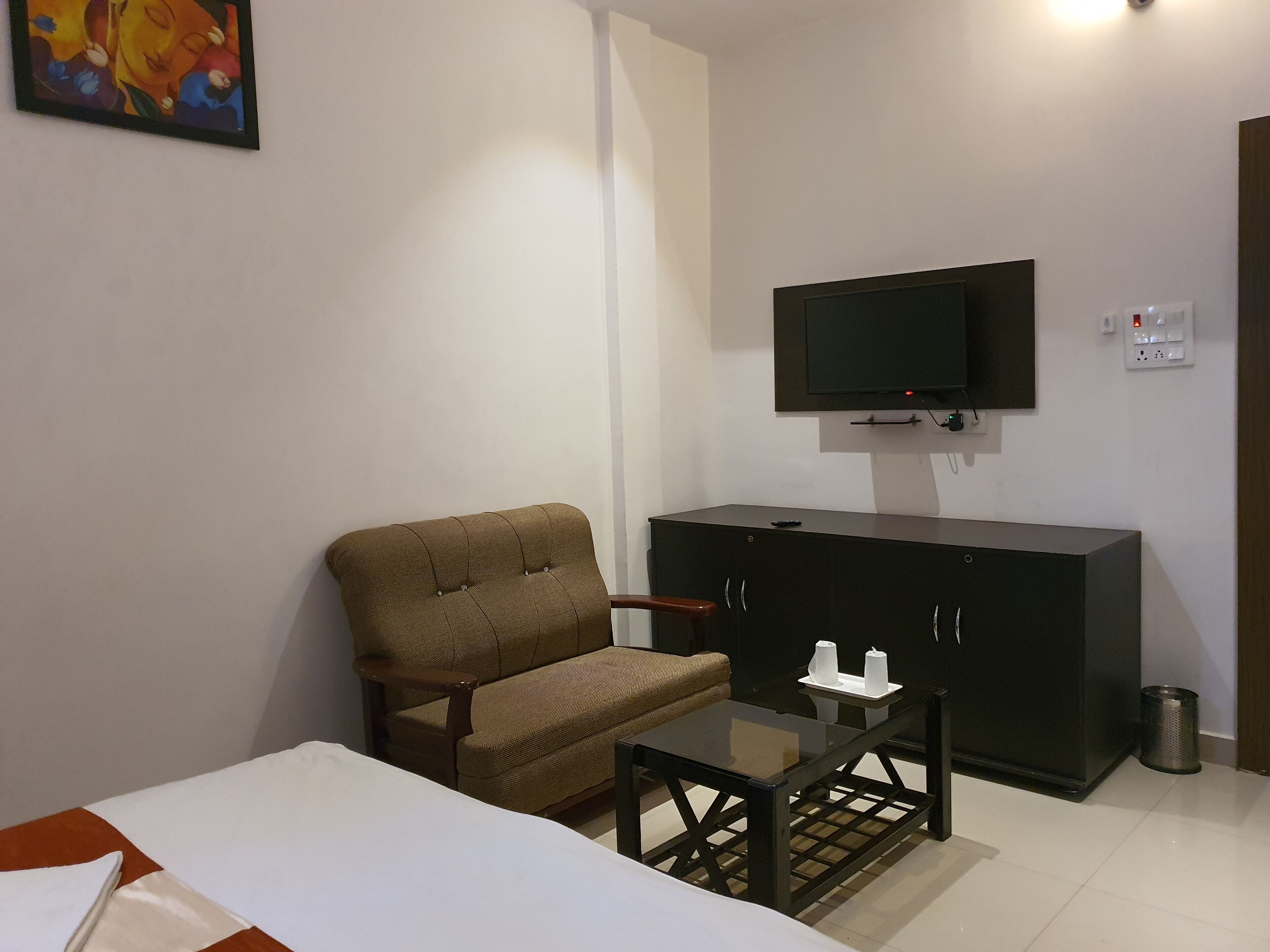 Une chambre d’hôtel avec un lit, un fauteuil marron, une petite table, un téléviseur fixé au mur et un placard.