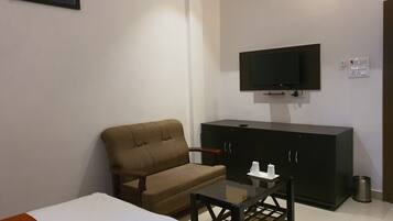 Une chambre d’hôtel avec un lit, un fauteuil marron, une petite table, un téléviseur fixé au mur et un placard.
