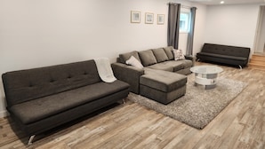 A modern living room with a sectional sofa, a smaller sofa, and a glass coffee table. - Walk to the Falls & Attractions!
Modern, clean & comfortable 4 bedroom house (Niagara Falls)