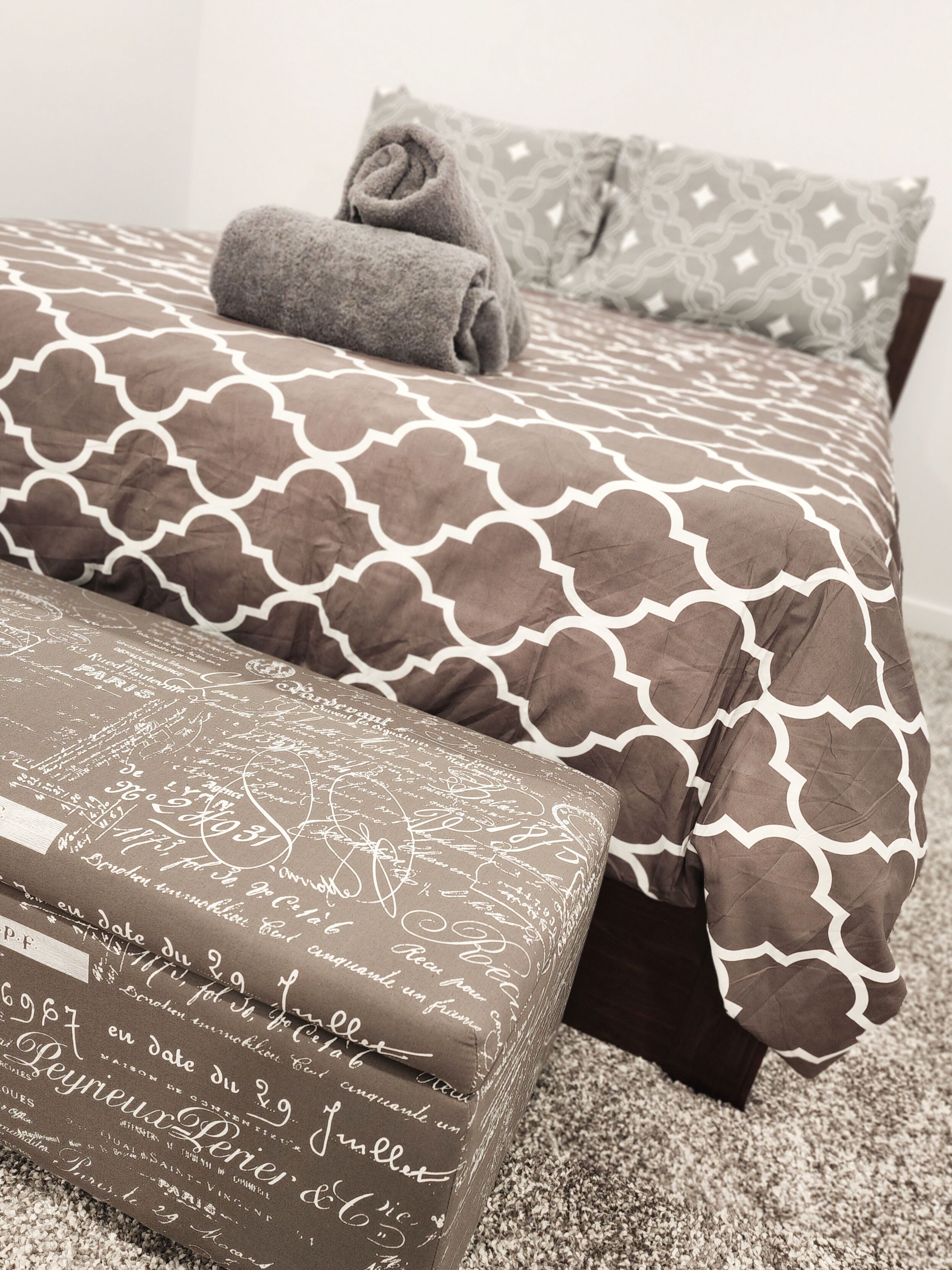 A bedroom with a patterned bedspread, pillows, and a bedside table with a decorative item.