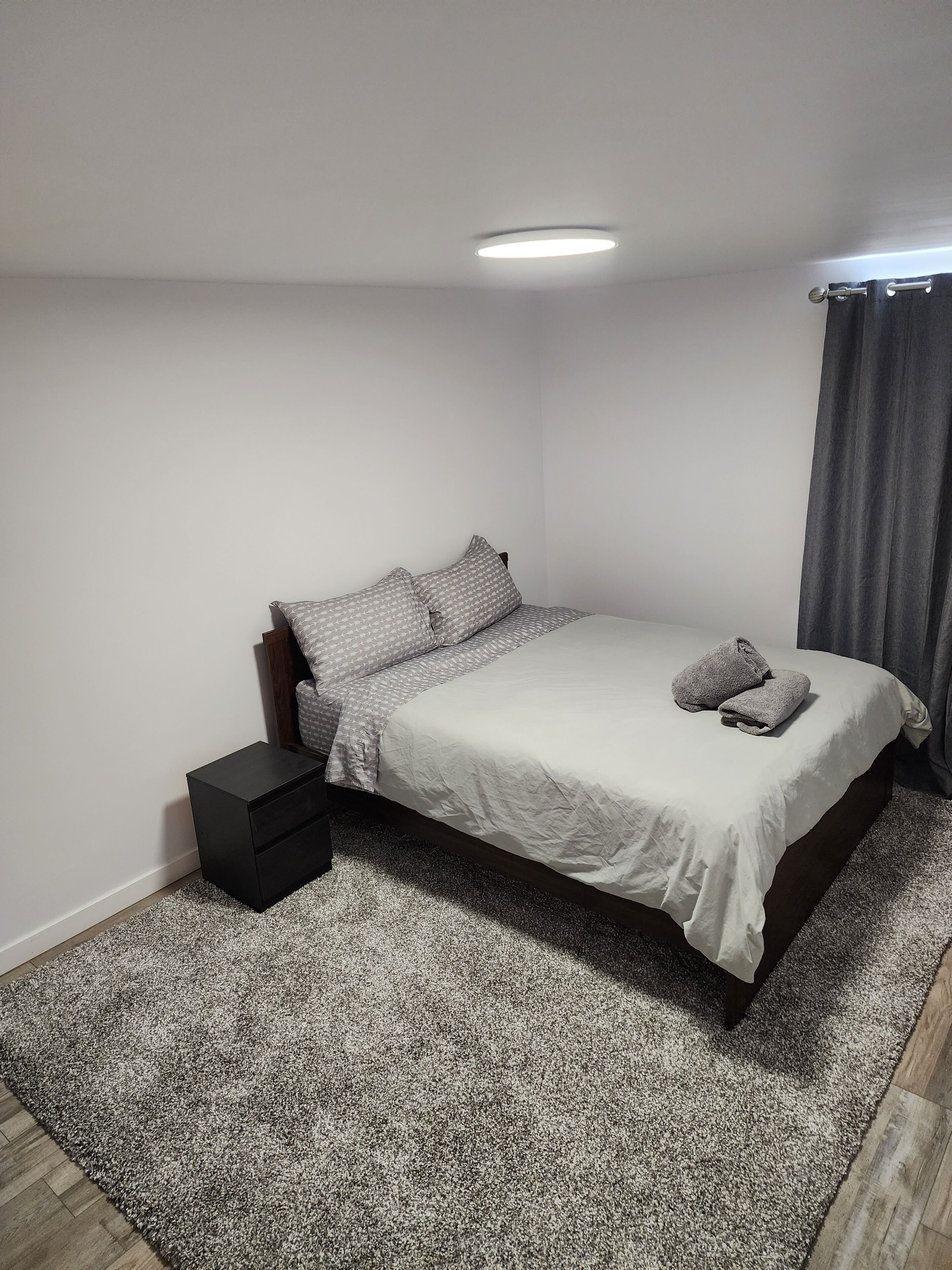 Un dormitorio con cama, mesita de noche, alfombra y lámpara de techo.