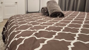 A neatly made bed with a patterned bedspread, a folded towel on the bed, a door, and a coat rack with a coat in the background. - Walk to the Falls & Attractions!
Modern, clean & comfortable 4 bedroom house (Niagara Falls)