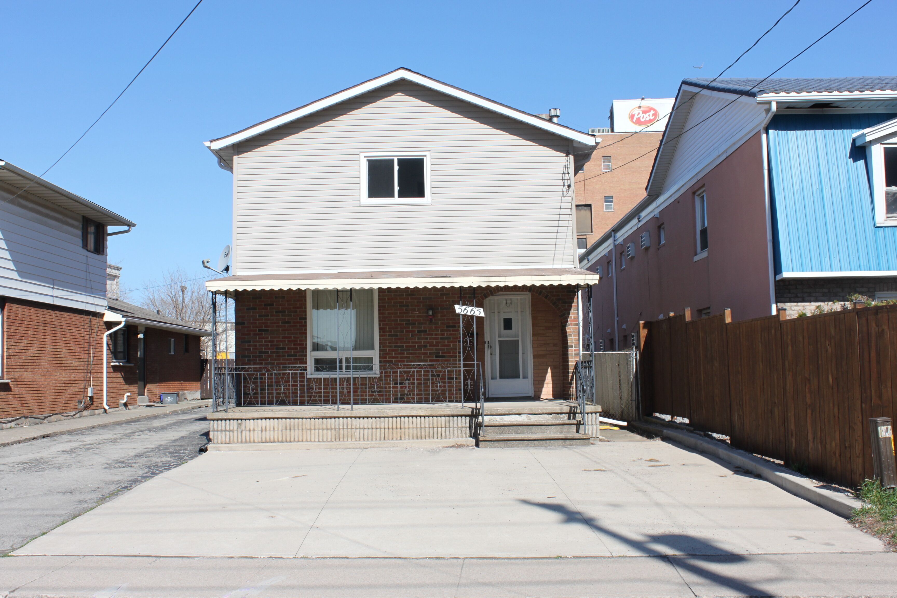 A two-story residential house with a front porch, a brick facade, and a small front yard.