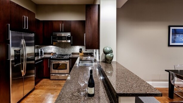 A modern kitchen with stainless steel appliances, a granite countertop, and a wine bottle.