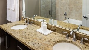 A bathroom with two sinks, a large mirror, and a towel rack with folded towels.