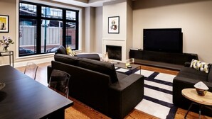 A modern living room with a fireplace, a flat-screen TV, and a large window offering a view of the outside.