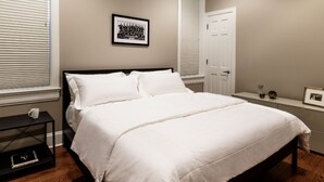 A bedroom with a bed, a nightstand, a framed picture, and a door.