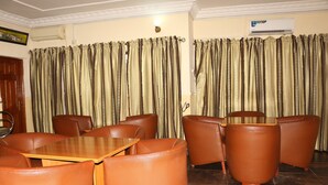 A room with a dining table and chairs, a sofa, curtains, and an air conditioning unit. - Xcape Hotels and Suites Ltd (Calabar)