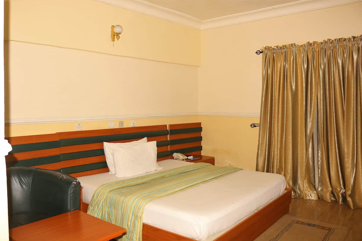 A hotel room with a bed, bedside table, lamp, and curtains.