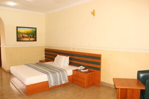 A hotel room with a bed, bedside table, and a painting on the wall. - Xcape Hotels and Suites Ltd (Calabar)