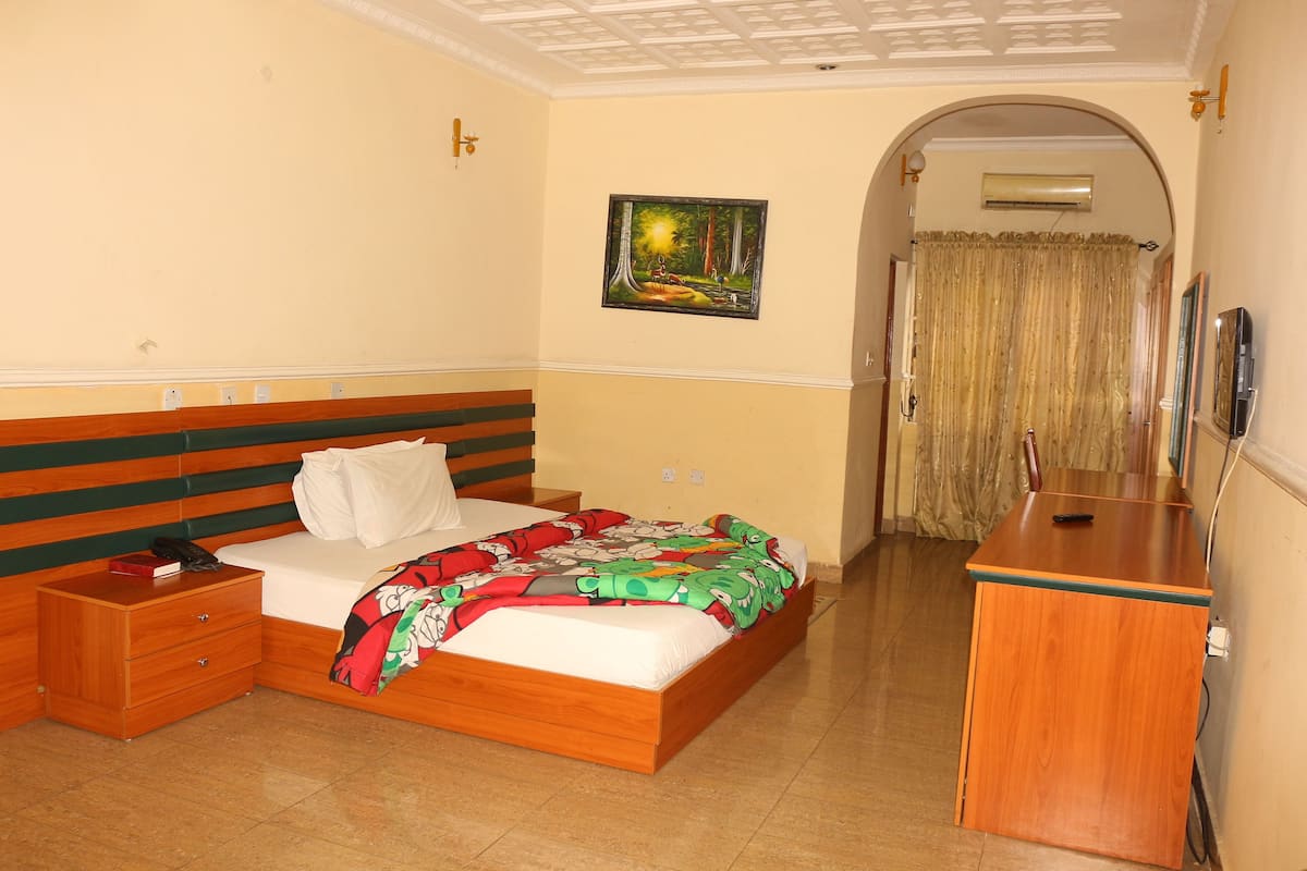 A bedroom with a bed, a nightstand, a wooden dresser, a painting, and an arched doorway.