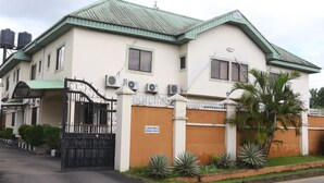 A two-story house with a gated entrance, air conditioning units, and a sign indicating it is a housing estate. - Xcape Hotels and Suites Ltd (Calabar)