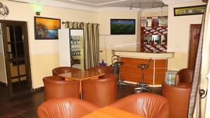A dining area with leather chairs, a wooden table, a bar with a wine rack, and a television on the wall. - Xcape Hotels and Suites Ltd (Calabar)