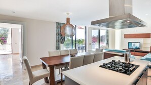 Eine moderne Küche mit einer zentralen Kochinsel, einem Essbereich mit Stühlen und einem Wohnbereich mit Sofa und Fernseher.