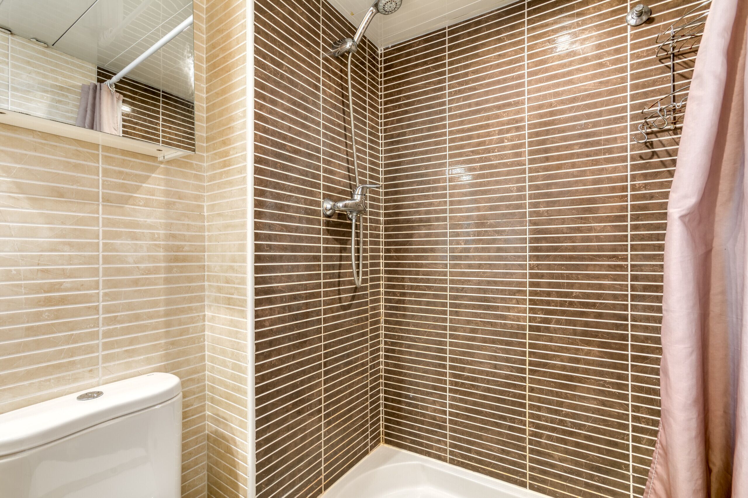 A corner shower with a tiled wall, a white bathtub, and a visible toilet.