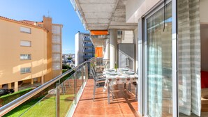 A balcony with a table set for dining, a glass railing, and a view of neighboring buildings. - MARINES MESTRAL  2 5 Roses (Rosas / Roses)