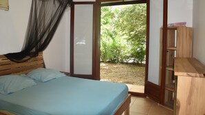 Un dormitorio con cama, mosquitero y puerta abierta que da a un jardín.