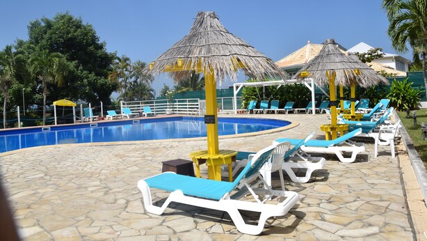 Un área de piscina con sillones de descanso y sombrillas de paja.