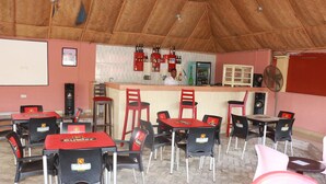 A restaurant with red and black chairs, a bar area, and a projector screen on the wall.