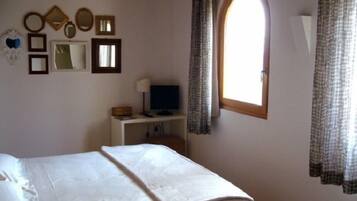 Ein Schlafzimmer mit einem Bett, einem Schreibtisch mit Computer, einem Fernseher und einem Fenster mit Vorhängen.