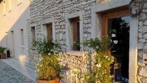 Edifici de pedra amb carrer pavimentat, plantes en testos i un fanal.