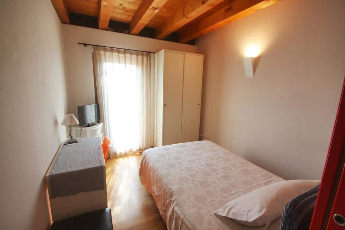 A bedroom with a bed, a desk with a lamp, a television, and a wardrobe.