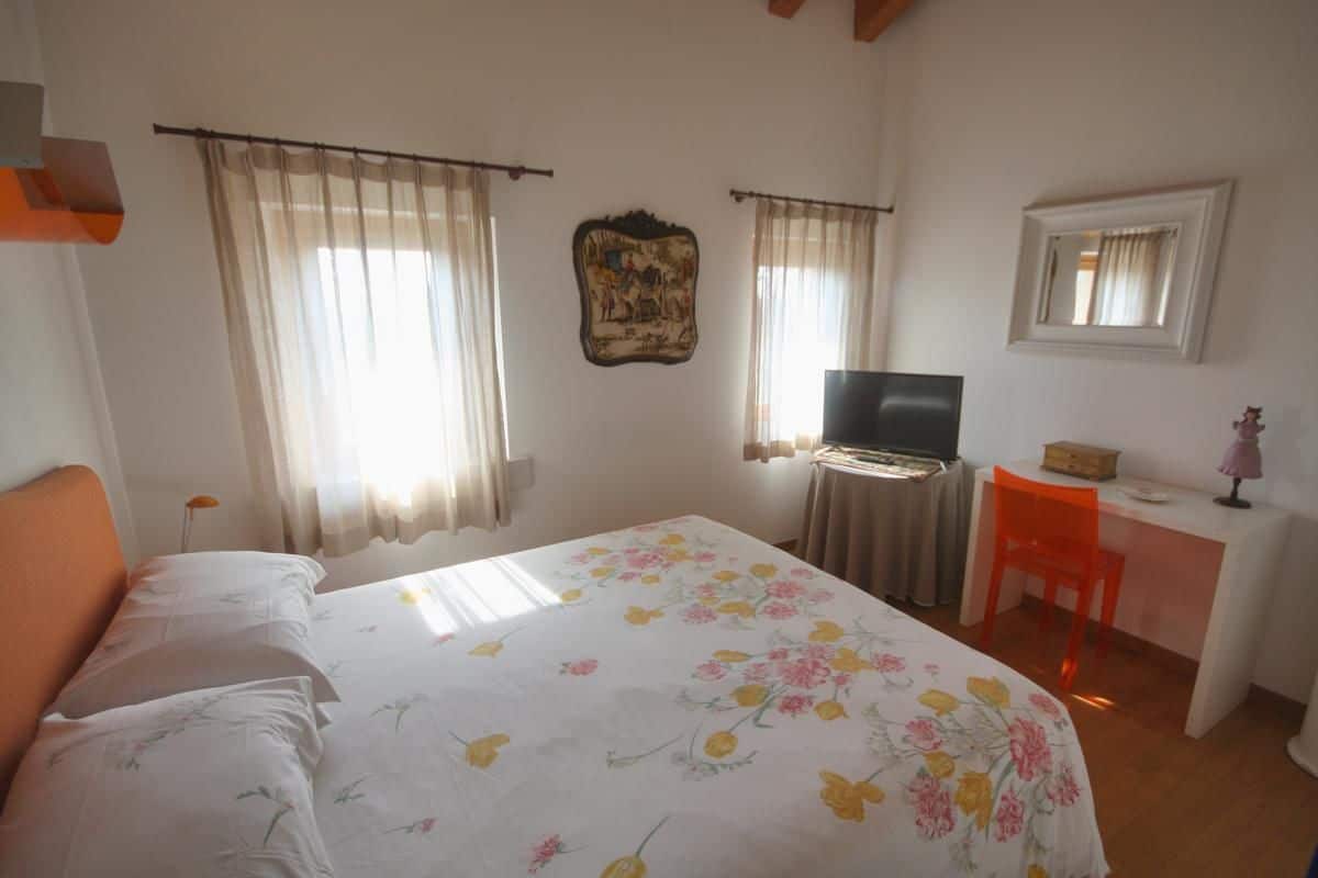 A bedroom with a bed, a desk, a chair, a television, and curtains.
