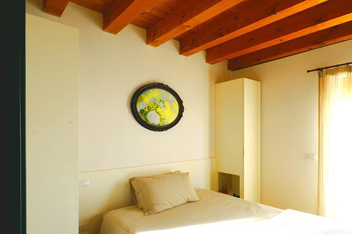 A bedroom with a bed, a wall-mounted mirror, and a circular painting.