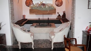 Un saló acollidor amb dues butaques blanques, una taula baixa de fusta i una peça decorativa a la paret.