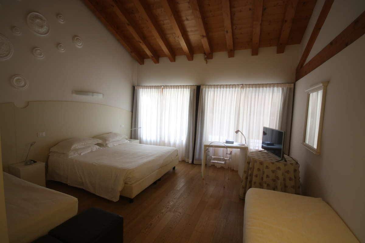 A bedroom with two beds, a desk with a chair, a television, and a window with curtains.