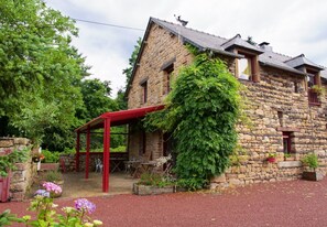 A stone building with a red-roofed pavilion, surrounded by greenery and potted plants. - Hôtel Jouet (Plelan-le-Grand)