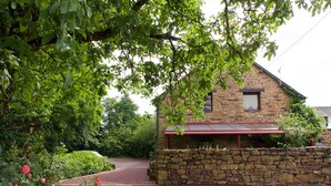 A stone building with a red roof, surrounded by lush greenery and a gravel driveway. - Hôtel Jouet (Plelan-le-Grand)