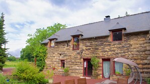 A stone building with a red door, a covered outdoor seating area, and a dirt path leading to the entrance. - Hôtel Jouet (Plelan-le-Grand)