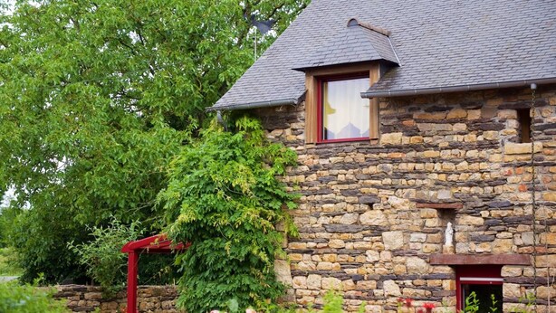 A stone building with a sloped roof, a small window with a red frame, and a red door. - Hôtel Jouet (Plelan-le-Grand)