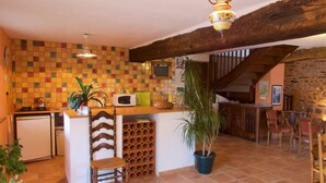 A kitchen with a tiled backsplash, wooden beams, a bar area, and a dining space with chairs. - Hôtel Jouet (Plelan-le-Grand)