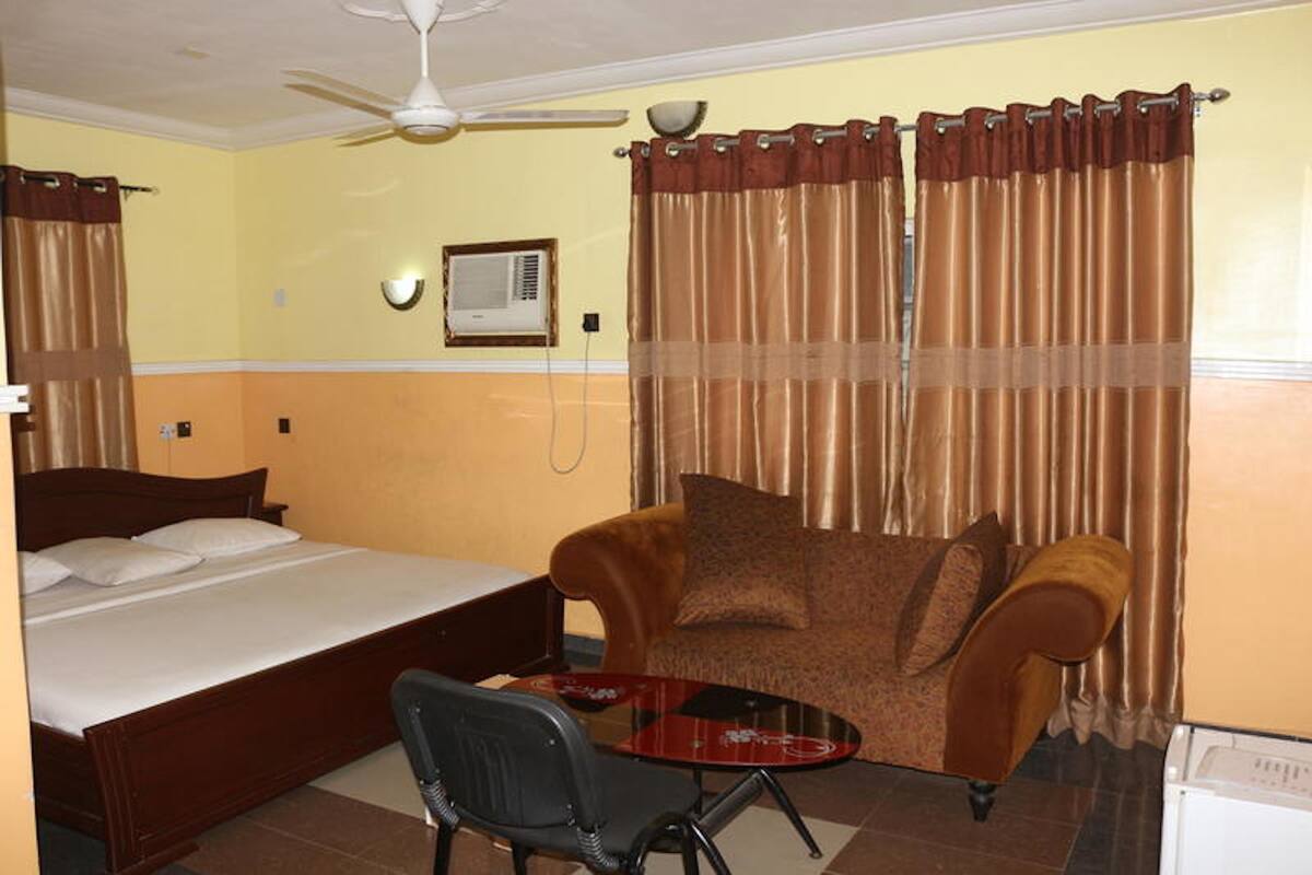 A hotel room with a bed, a chair, a table, a ceiling fan, and curtains.