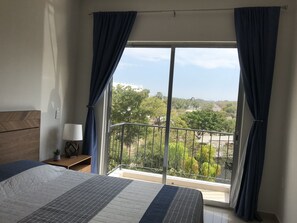 Relax in this serene bedroom with a large bed and a balcony offering a view of the surrounding green landscape.