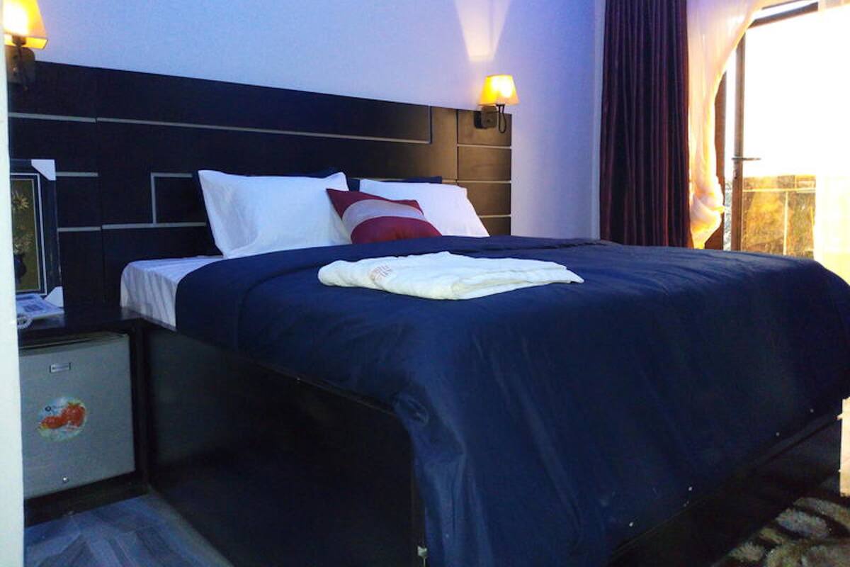 A hotel room with a bed, nightstand, lamp, and curtains.
