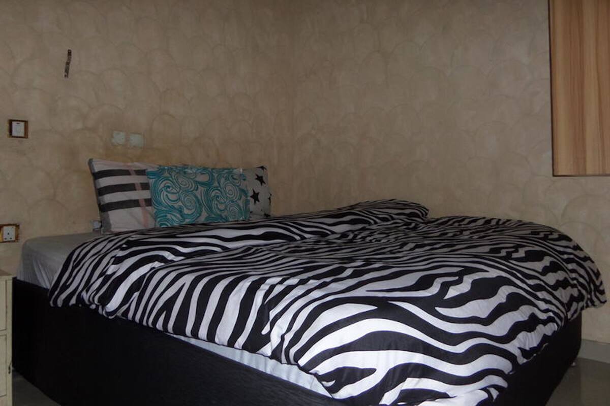 A bedroom with a zebra-striped bedspread, a patterned pillow, and a plain wall.