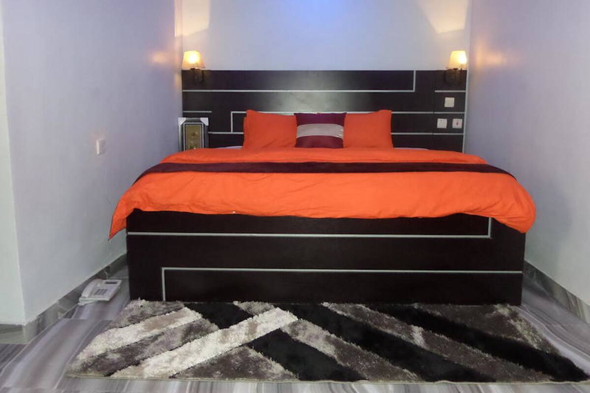 A bedroom with a black headboard, orange bedding, and a patterned rug.