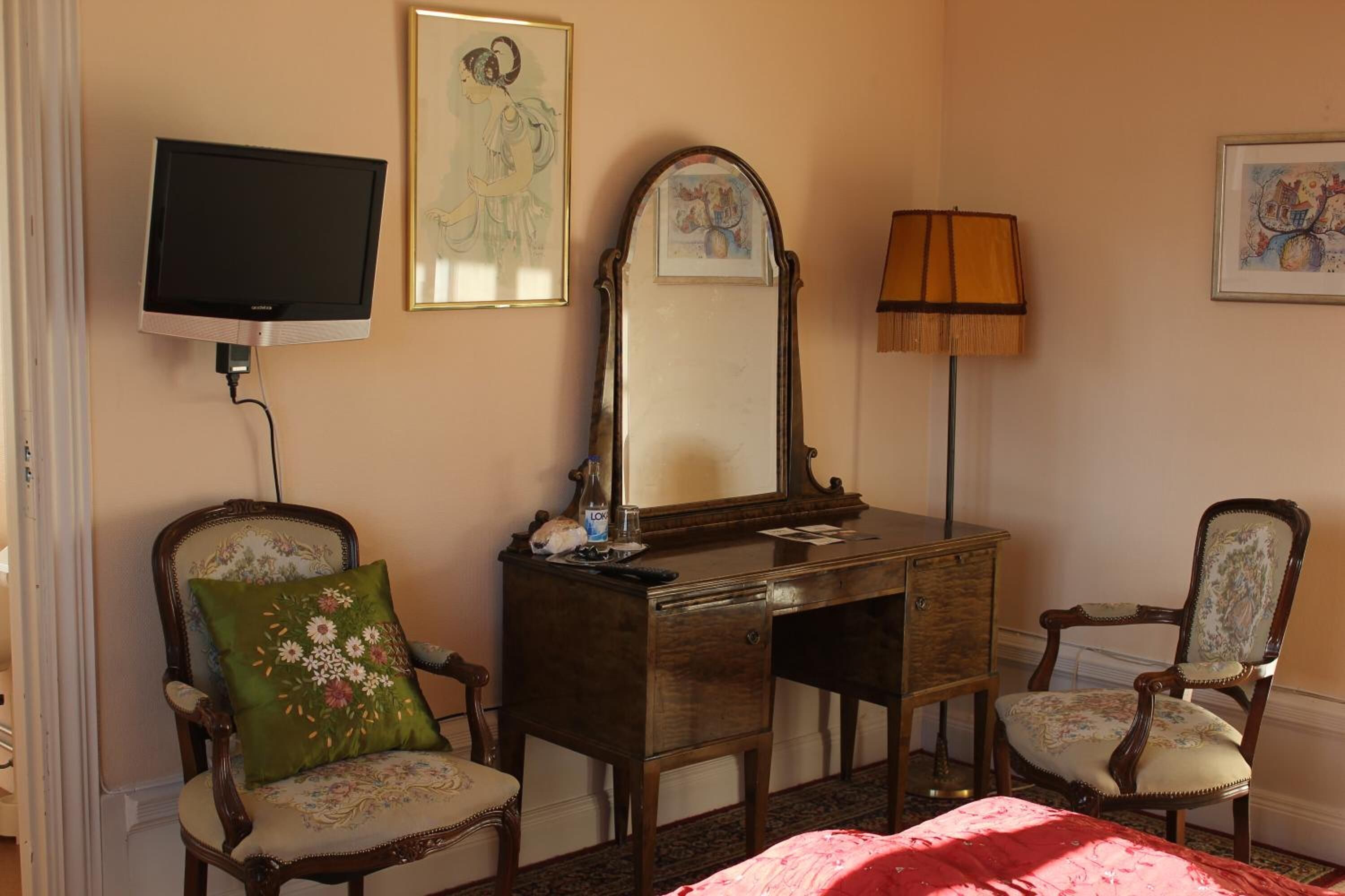 Een kamer met een houten bureau, twee stoelen, een televisie en een spiegel.