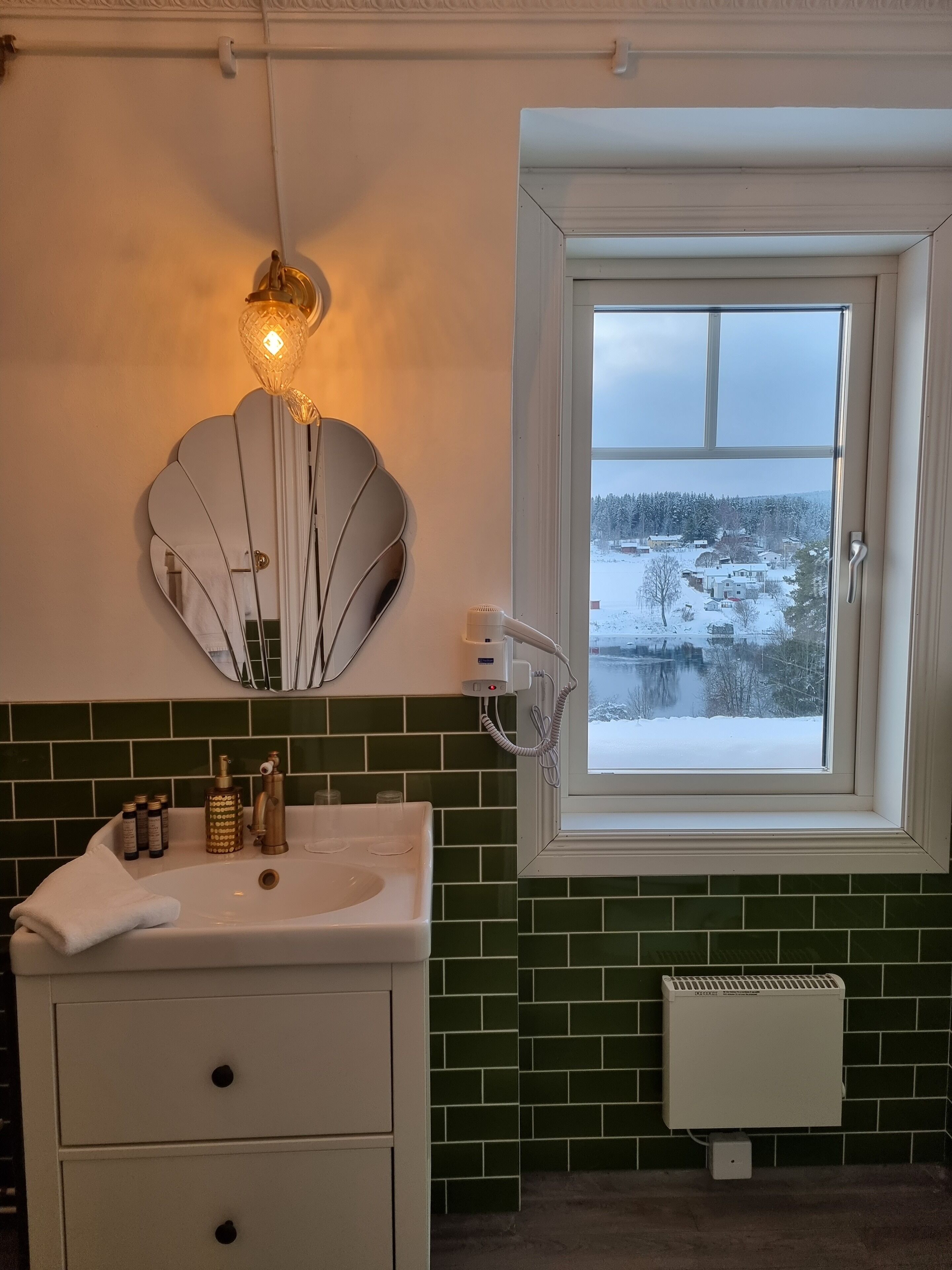 A bathroom with a white sink, green tiled backsplash, a large mirror, and a window with a snowy view.