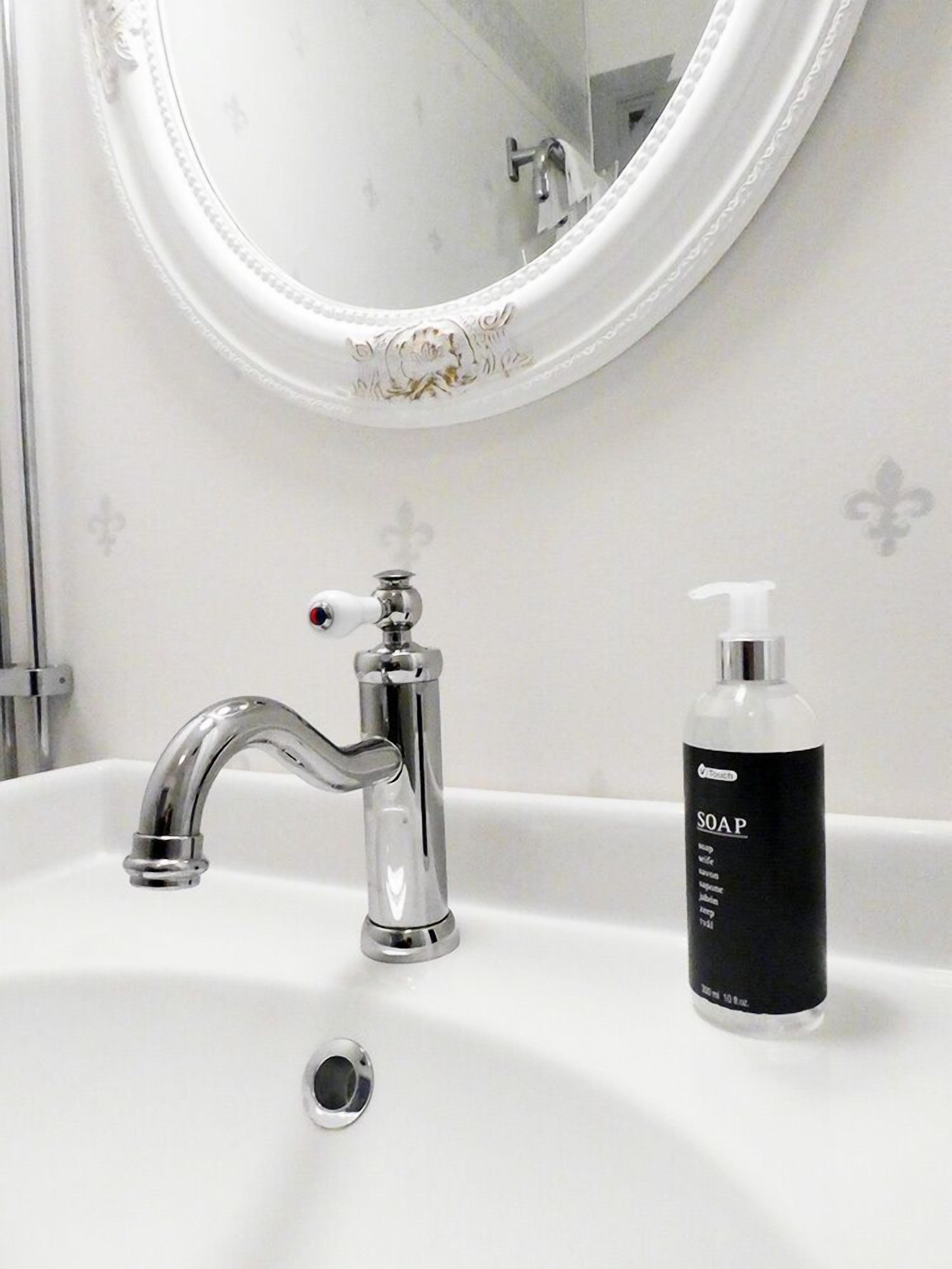 A bathroom with a white sink, a chrome faucet, and a soap dispenser.