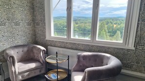 A room with two armchairs, a small round table, and a view of a lake and forest through a large window.