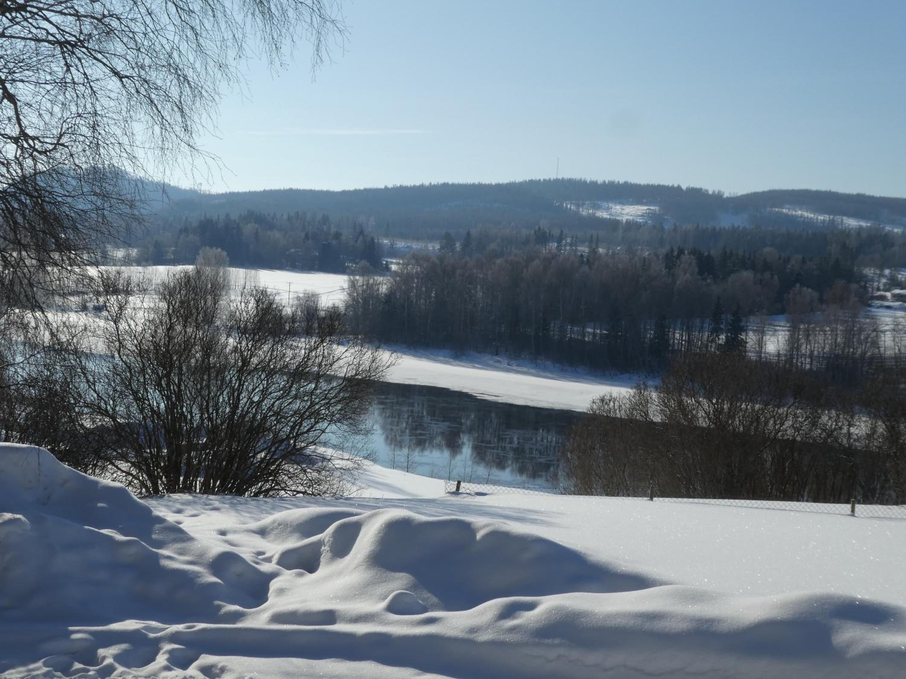 A snow-covered landscape with a frozen lake and trees in the background.