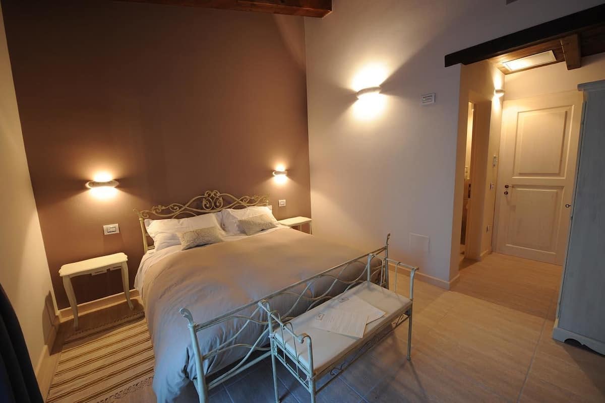Un dormitorio con estructura metálica para la cama, una mesita de noche y dos luces fijadas a la pared.